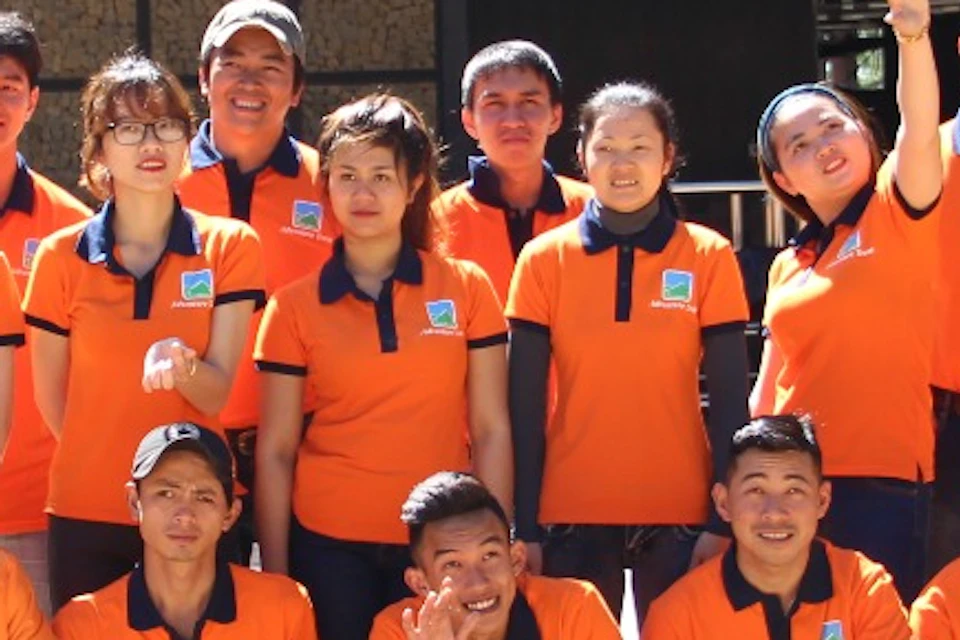 A group of people wearing orange shirts posing together outdoors in front of a building with a tiled patio.
