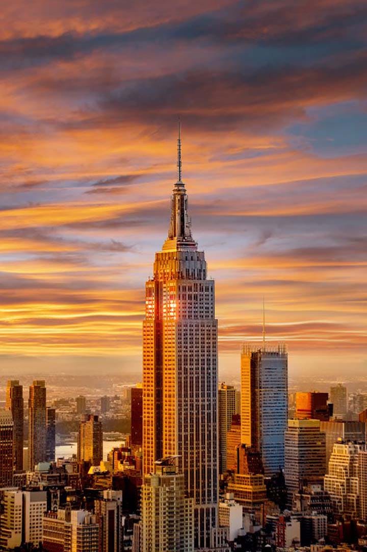 The Empire State Building at sunset with a skyline backdrop and dramatic, colorful clouds.