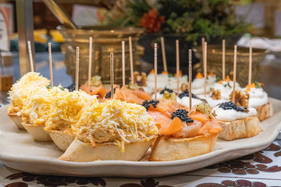 A plate of assorted bite-sized appetizers on bread slices, topped with various ingredients like cheese, salmon, and caviar.