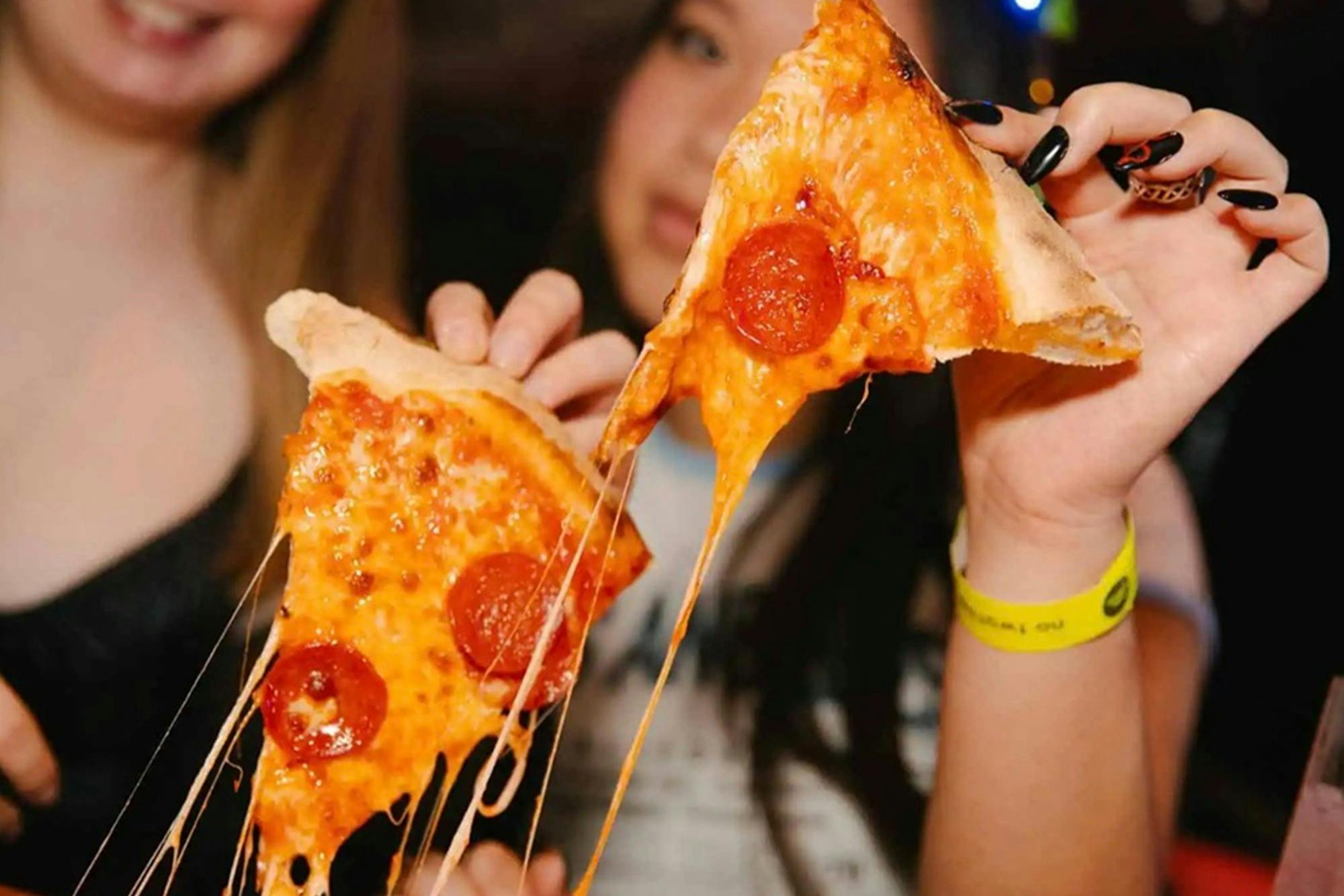 Two people holding slices of pepperoni pizza with melted cheese stretching between them.