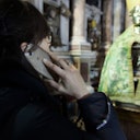 Person holding a phone to their ear and facing an ornate statue draped in green fabric inside a building with columns.