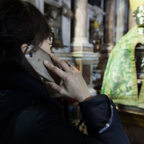 Person holding a phone to their ear and facing an ornate statue draped in green fabric inside a building with columns.