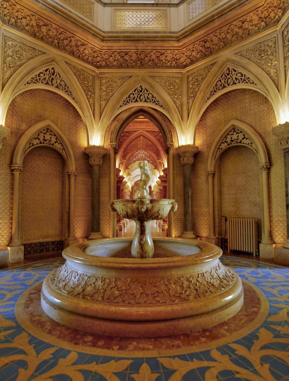 Ornate indoor scene with arched doorways, intricate designs, and a central fountain under warm lighting.