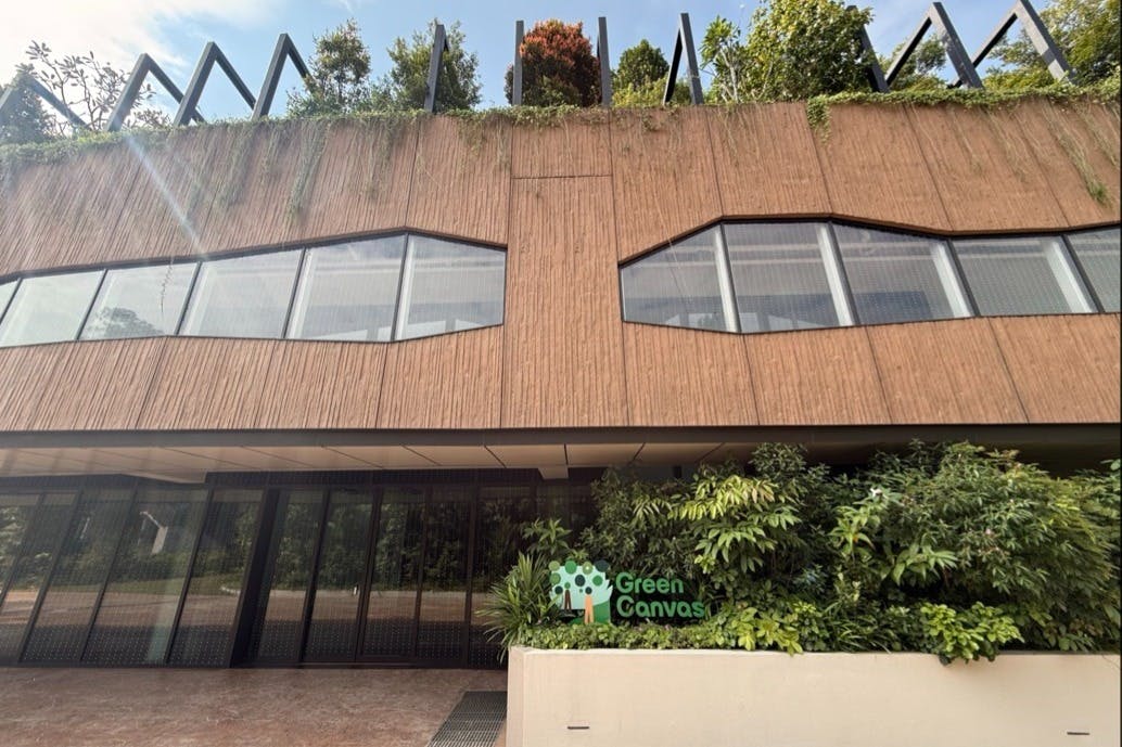 목재 패널, 커다란 창문, 녹지, '그린 캔버스' 라고 적힌 간판이 있는 현대적인 건물 외관.