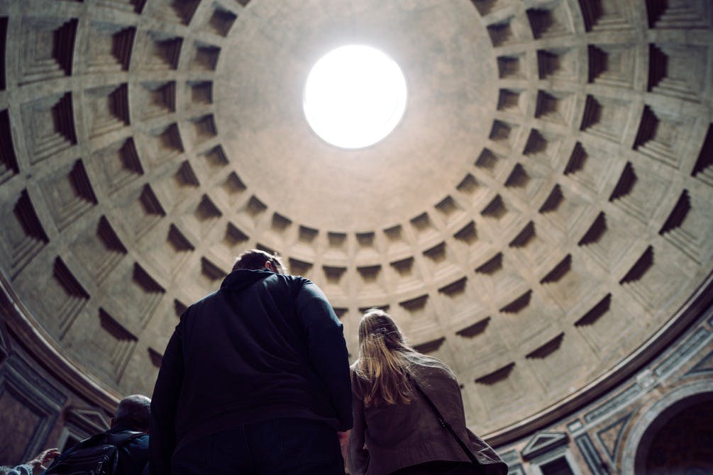 Due persone guardano un grande soffitto circolare a cupola con un oculo centrale, all'interno di una grande struttura architettonica.