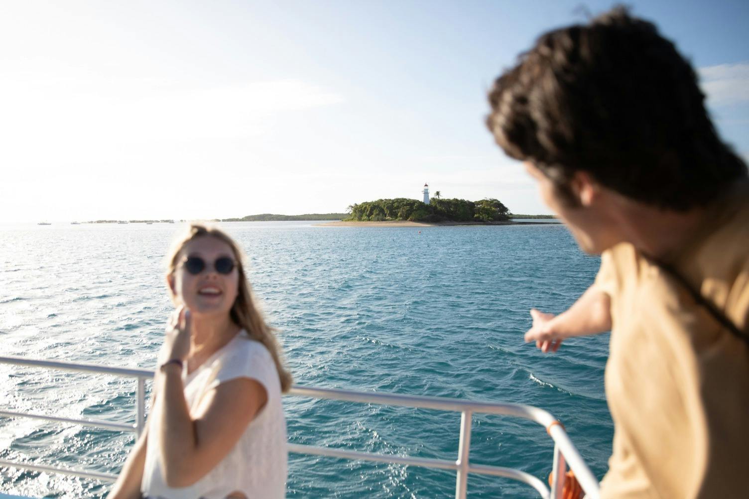 Due persone su una barca che puntano verso un&#39;isola lontana con un faro circondato da acqua blu sotto un cielo limpido.