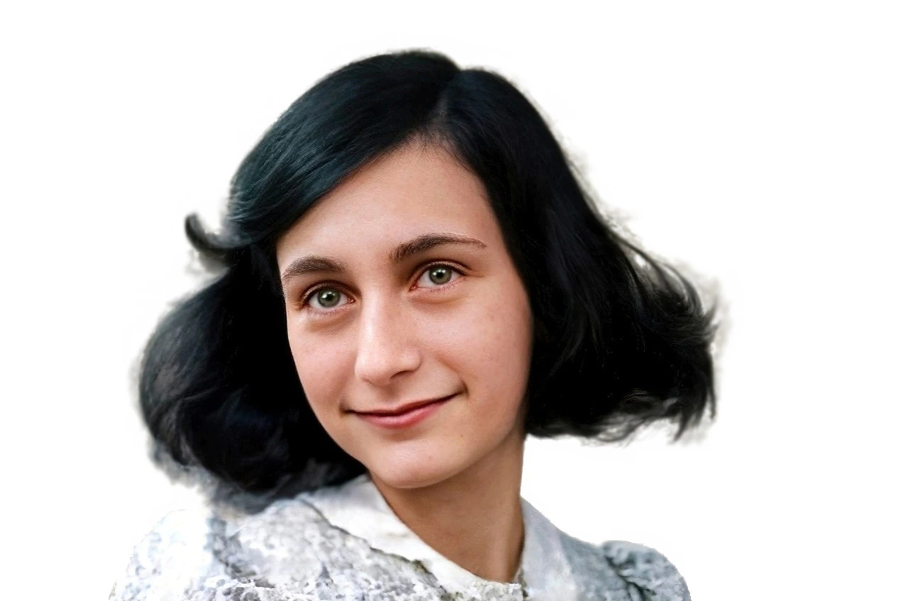 Young person with short, dark hair and green eyes smiling slightly. Wears a light-colored, lace-collared blouse. White background.