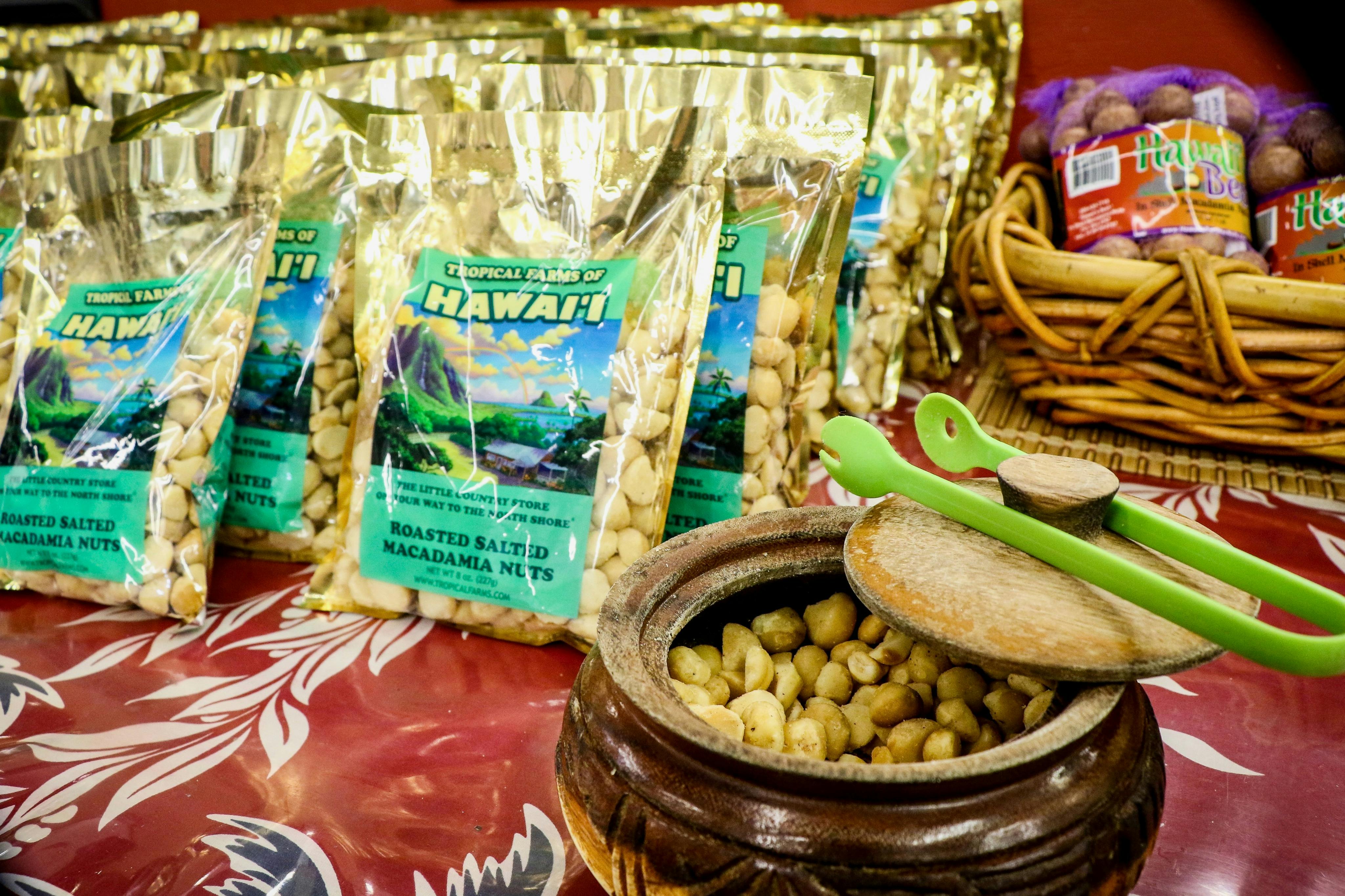 Bags of Tropical Farms of Hawaii roasted salted macadamia nuts displayed with an open wooden bowl of nuts and spoons.
