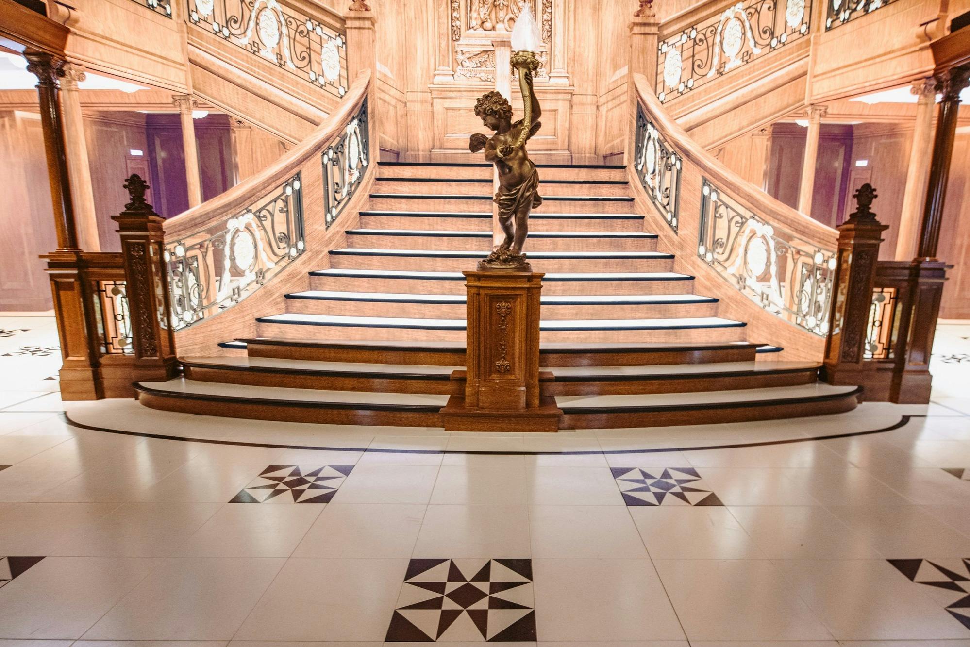 A grand wooden staircase with ornate railings and a statue holding a lamp on a pedestal at the base.