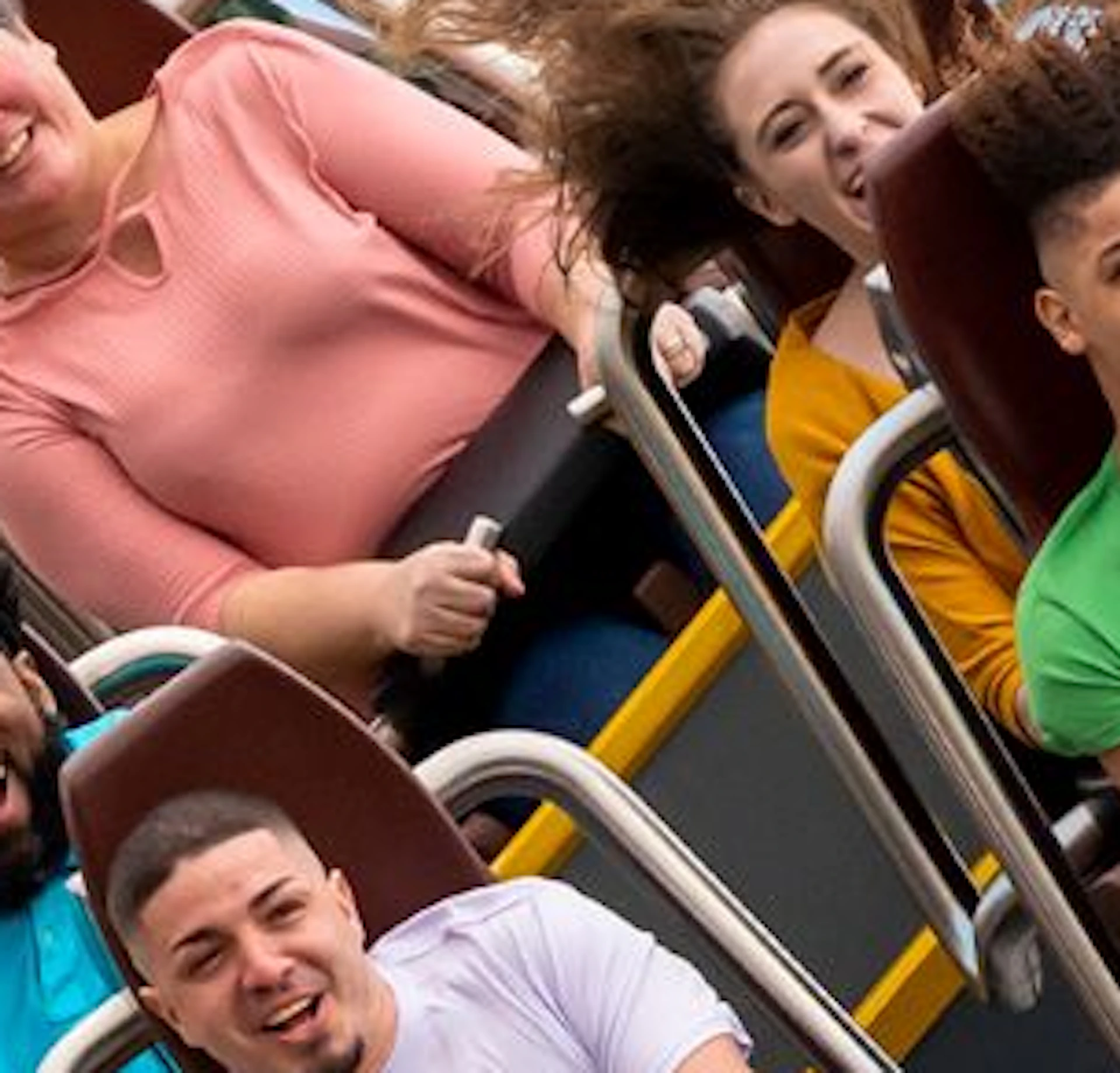 People on a rollercoaster ride down a steep curve with hands raised against a backdrop of blue sky and scattered clouds.