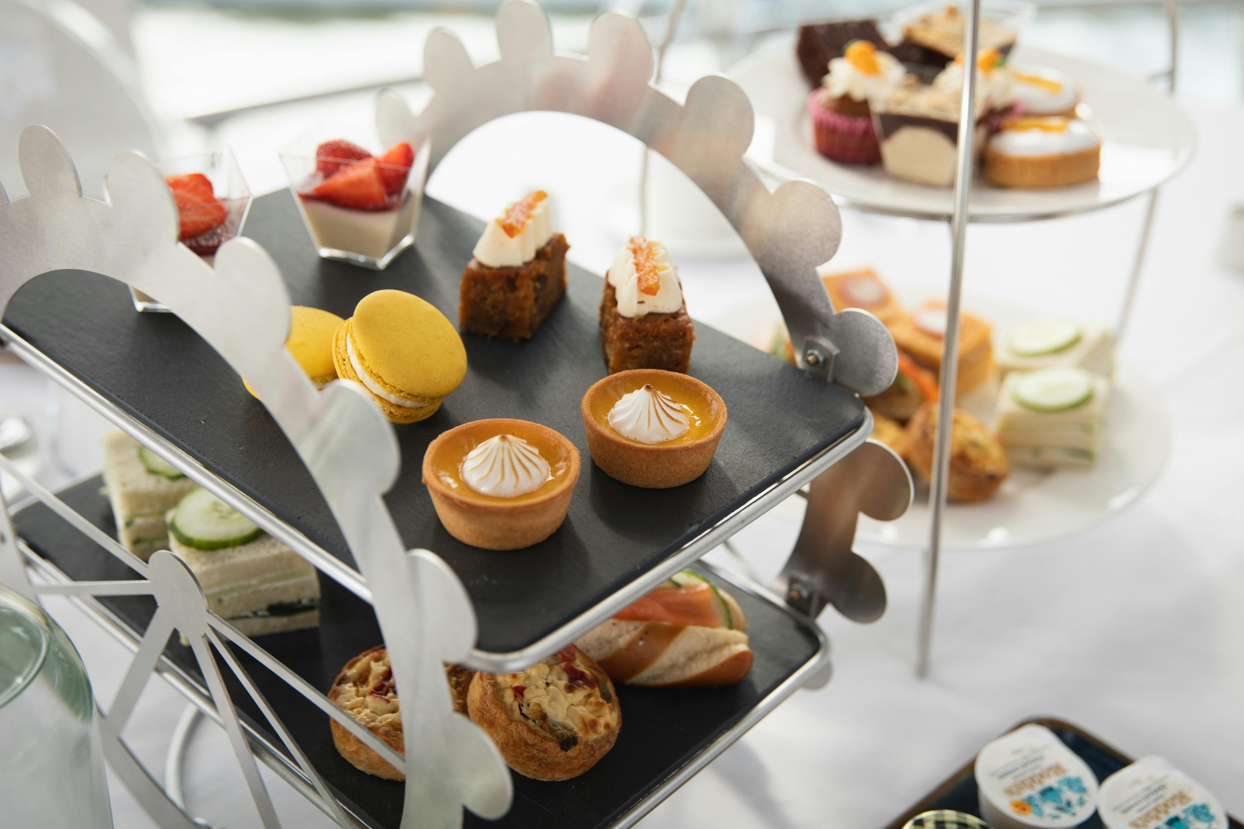 A tiered stand holding assorted desserts and pastries, including cakes, macarons, tartlets, and sandwiches.