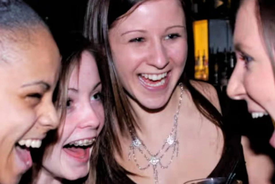 Four women laughing and holding drinks at a bar.