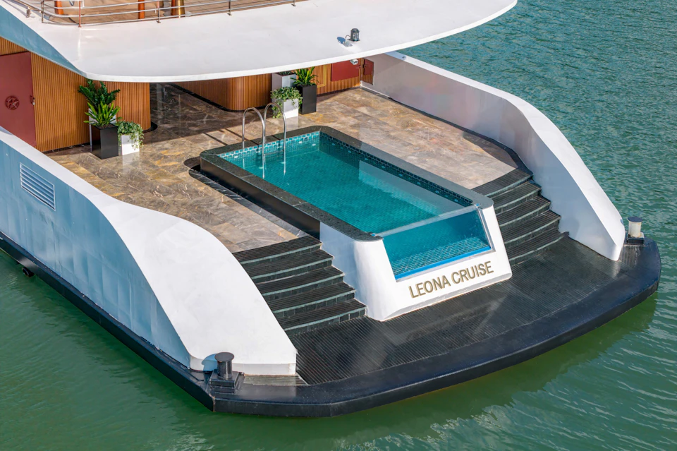 Rooftop pool on a yacht with marble tiles and steps leading into the water. The name "Leona Cruise" is displayed on the side.