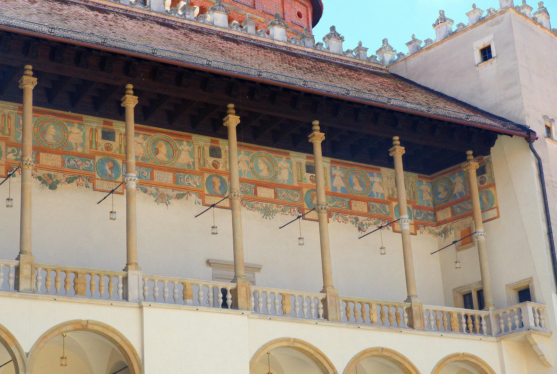 Ornate building facade with arched windows, decorative frescoes, and columns supporting a wooden roof, under a clear blue sky.
