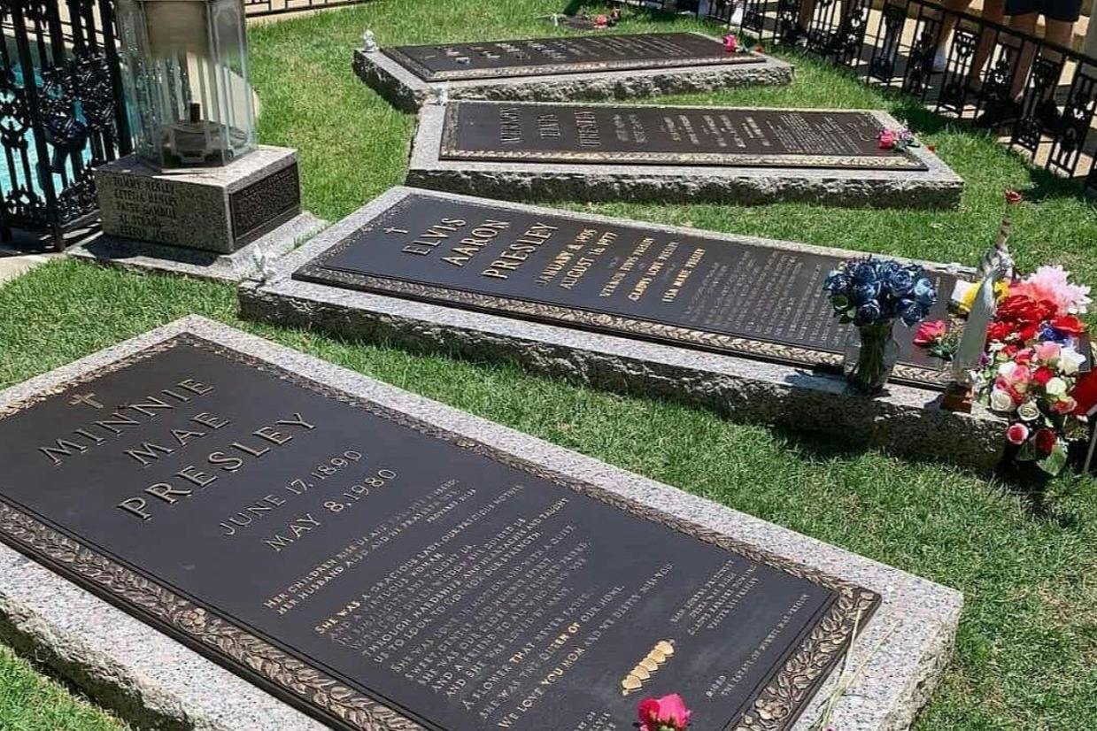 A set of grave markers on a neatly maintained lawn, with flowers placed near some of the plaques.