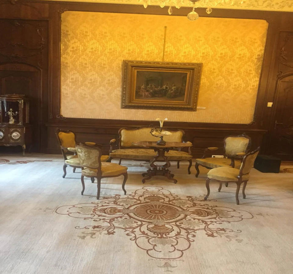 A vintage living room with elegant antique furniture, a detailed rug, ornate wallpaper, and a framed painting on the wall.