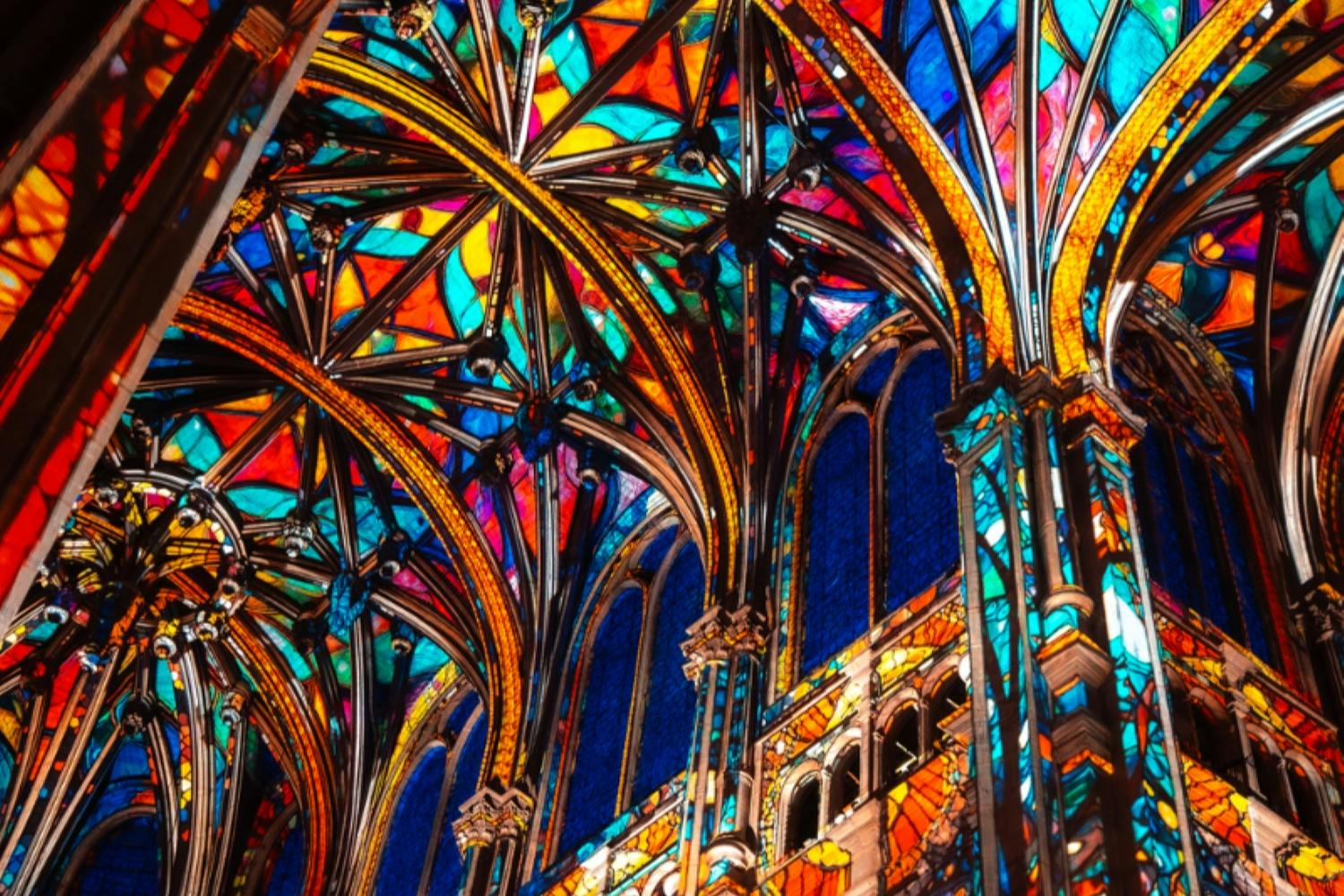 Intricate stained glass windows and colorful arched ceilings of a Gothic-style cathedral.