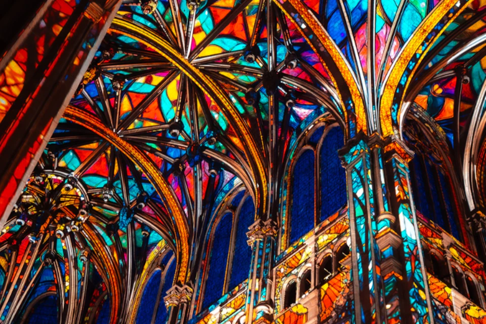 Intricate stained glass windows and colorful arched ceilings of a Gothic-style cathedral.