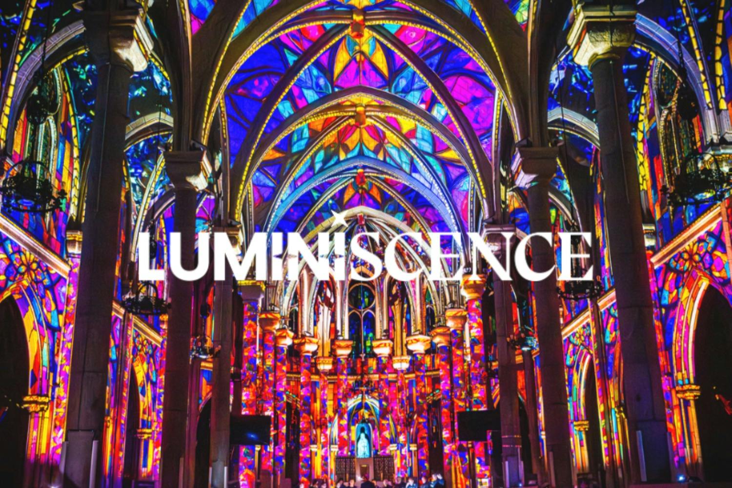 Intérieur d'une cathédrale où des projections lumineuses aux couleurs vives illuminent ses arcs et ses murs, sur lesquelles figure le mot « LUMINISCENCE ».