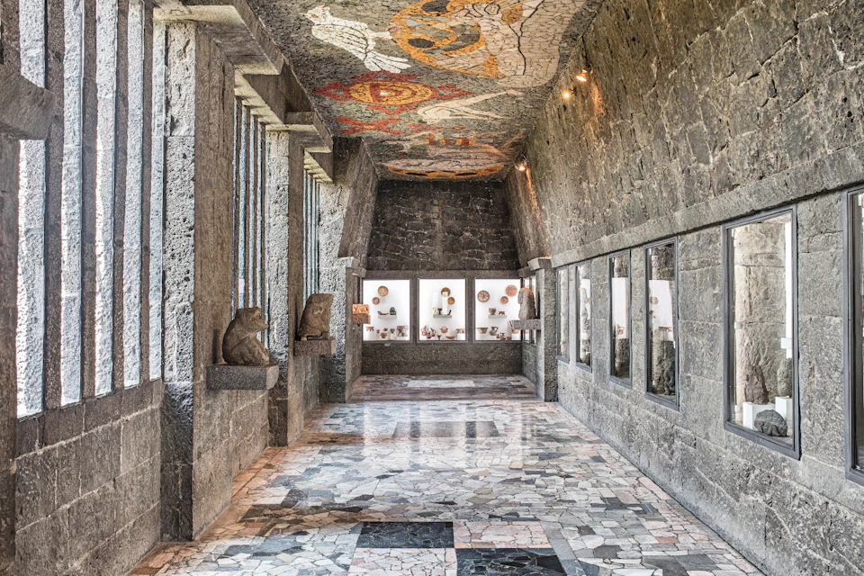 A stone-walled hallway with display cases of artifacts and a colorful mosaic ceiling depicting various designs.
