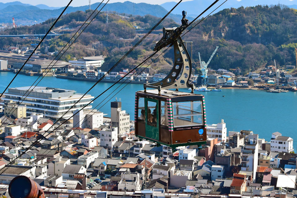 A cable car suspended over a cityscape with a river, buildings, and hills in the background.