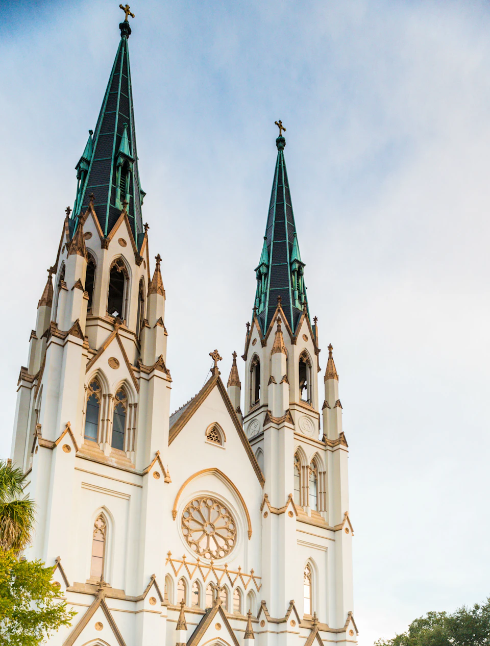 Twin green-roofed spires and arched windows of a cathedral against a blue sky with clouds.