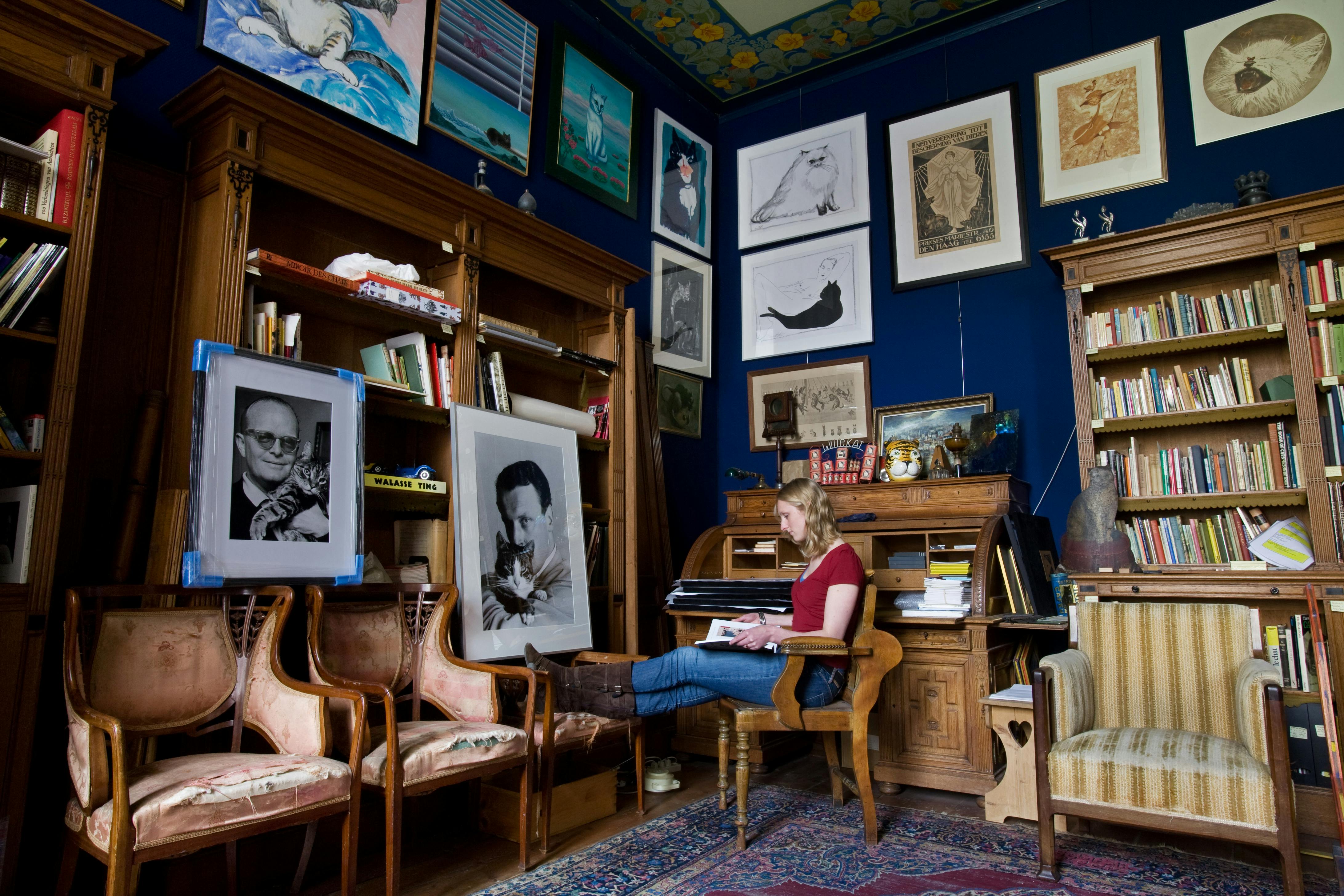 一位女士坐在一个不拘一格、充满艺术气息的房间里阅读一本书，周围环绕着相框、绘画和复古家具。