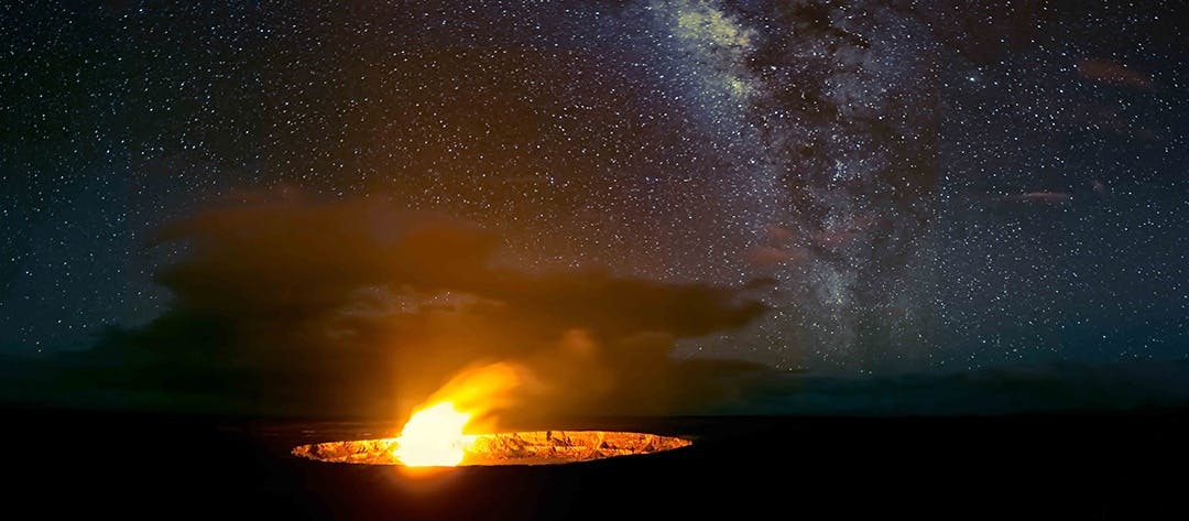 Un cràter de lava brillant sota un cel nocturn estrellat amb la Via Làctia visible.