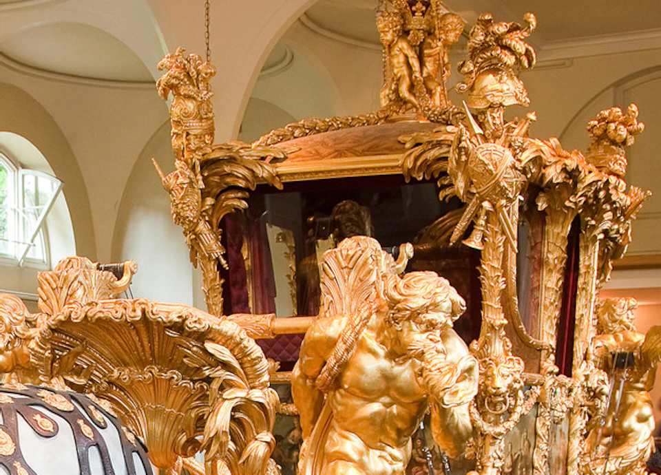 A family admires a large, ornate golden carriage inside a grand hall, led by a uniformed rider atop a white horse.