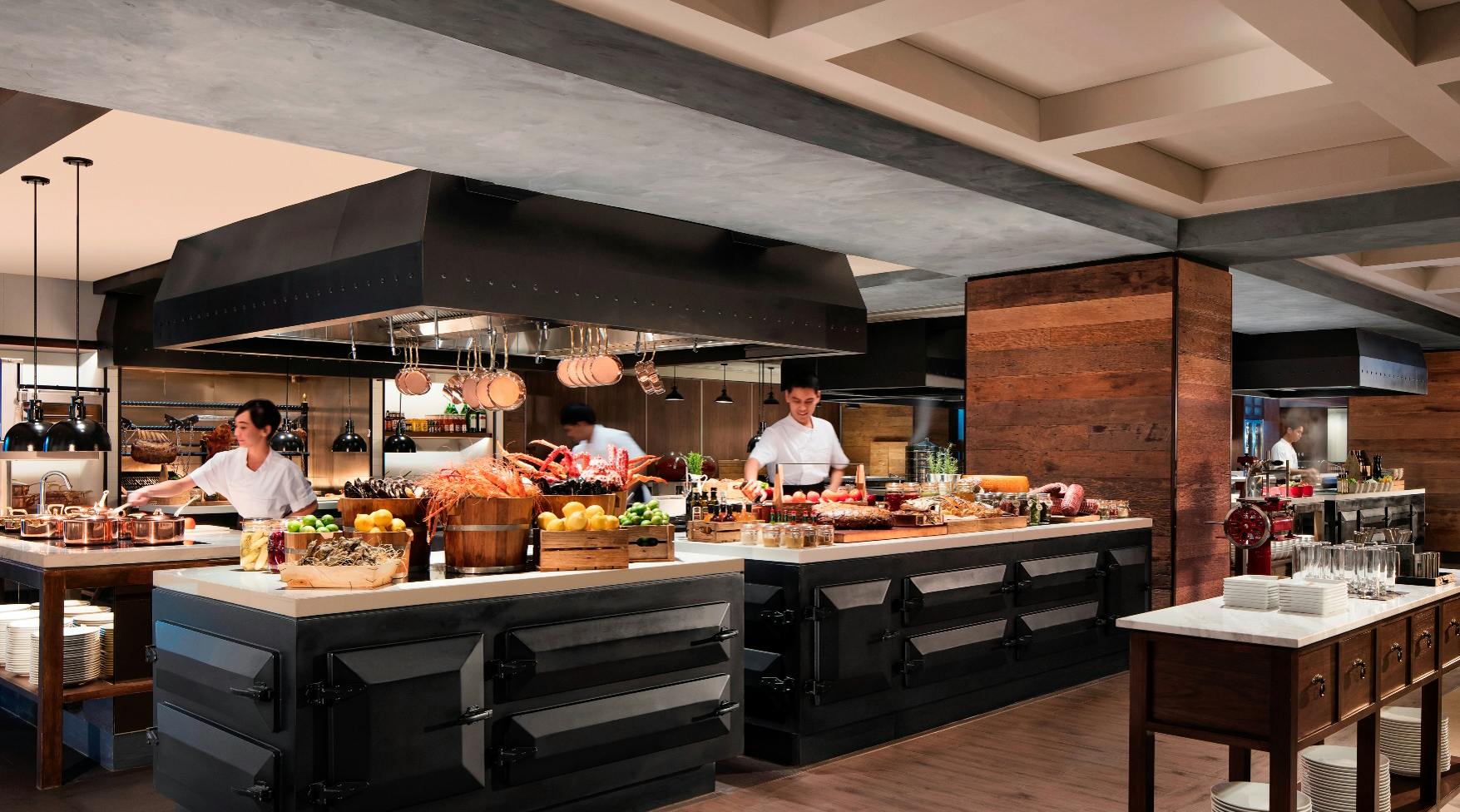 Chefs working in a professional kitchen with a variety of fresh ingredients and food displays on the counters.