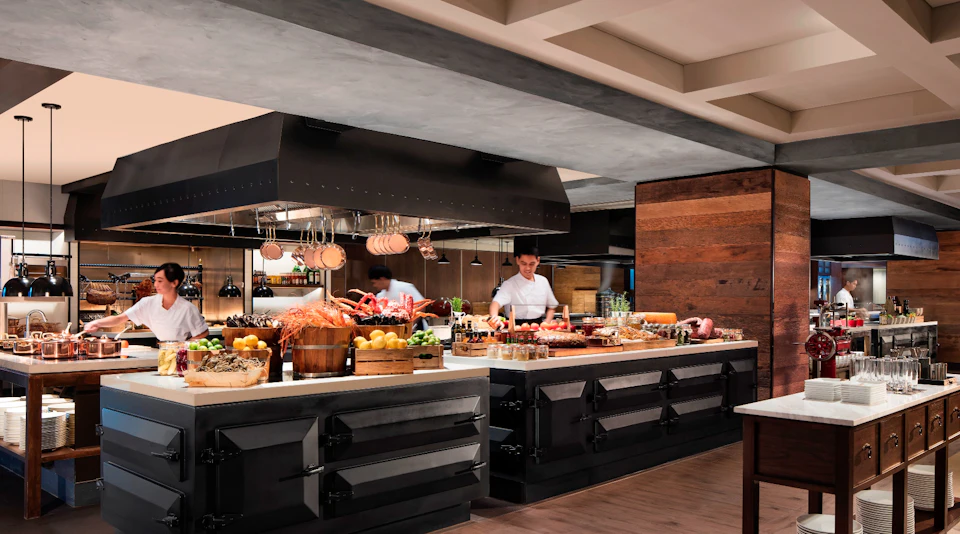 Chefs working in a modern kitchen with a variety of fresh ingredients and dishes displayed on counters.