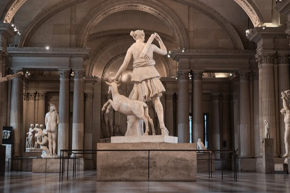 A marble statue of a woman with a deer in a museum gallery with columns and arched ceilings.