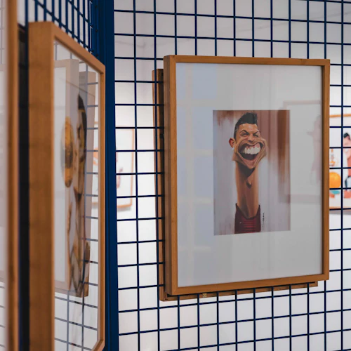 Inramade karikatyrer av människor som visas på blå rutnätspaneler i ett konstgalleri.