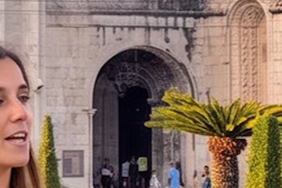 A guide speaks to tourists in front of a historic cathedral and garden during sunset.