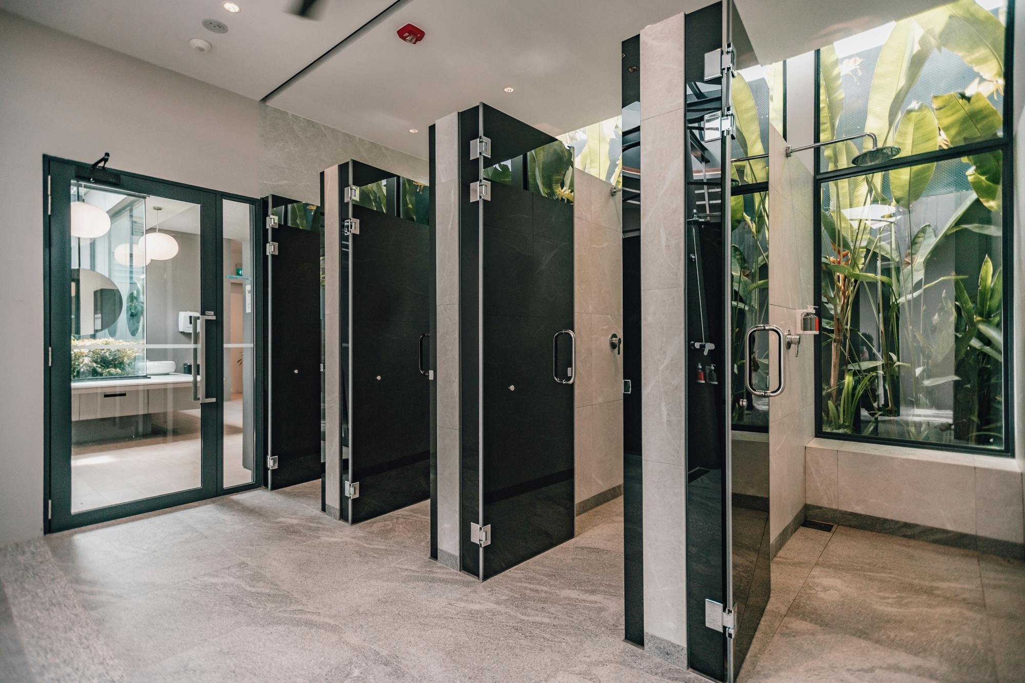 A modern restroom with glass-paneled shower stalls, sleek fixtures, and large windows letting in natural light.