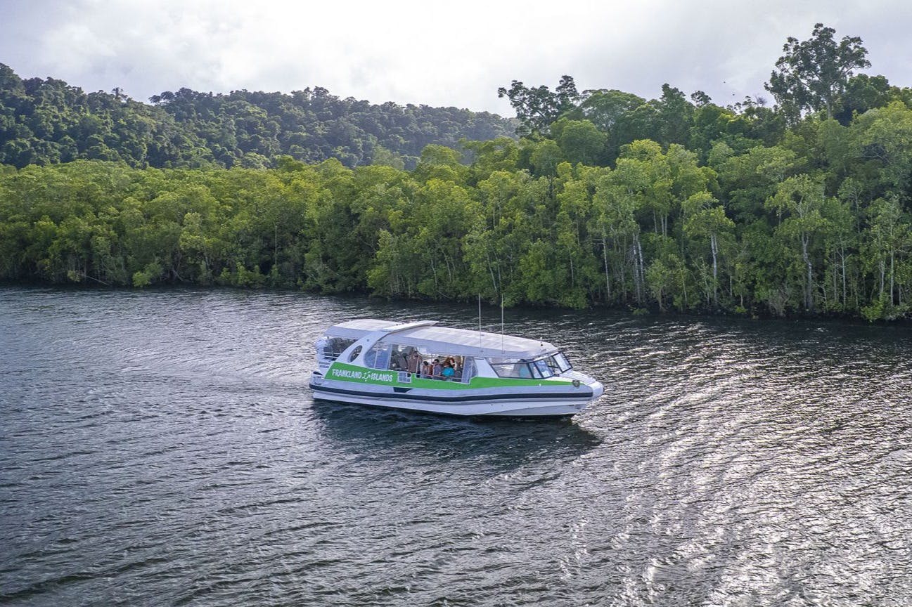 Zeleno-bílá loď s cestujícími pluje po řece vedle hustého zeleného lesa.