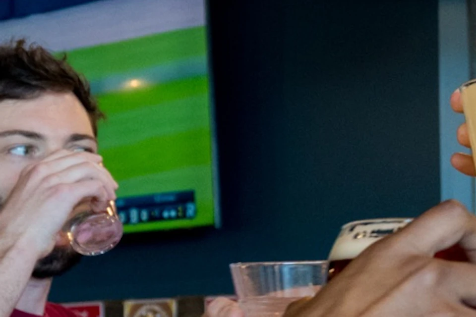 A group of people sitting at a bar table, clinking glasses, under warm lighting in a casual bar setting.