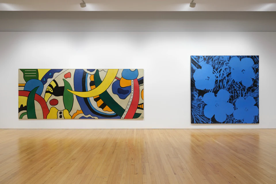 An art gallery with two large paintings on a white wall, one abstract and colorful, the other with blue flowers on a dark background.