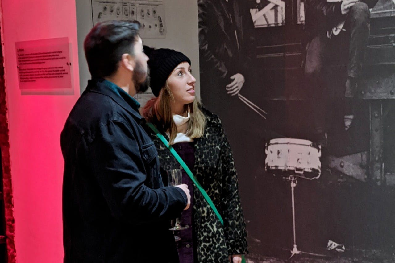 Due persone in abbigliamento casual guardano una mostra al chiuso con illuminazione rossa e foto in bianco e nero sulla parete.