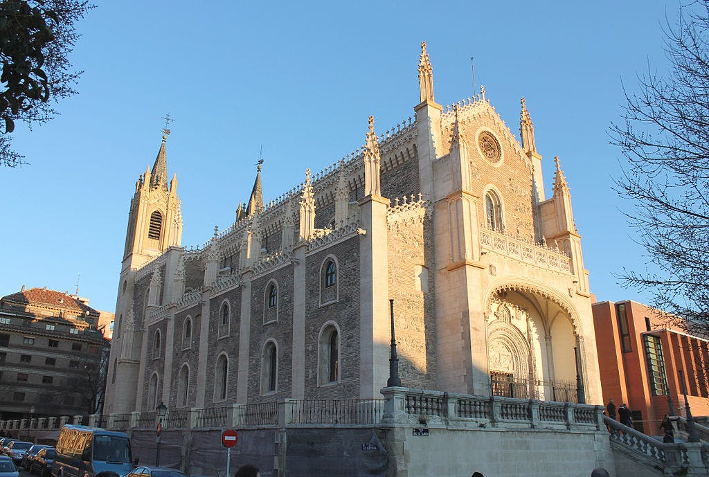 複雑な石細工、高い尖塔、アーチ型の入り口、澄んだ青い空の下を歩く人々がいるゴシック様式の教会。