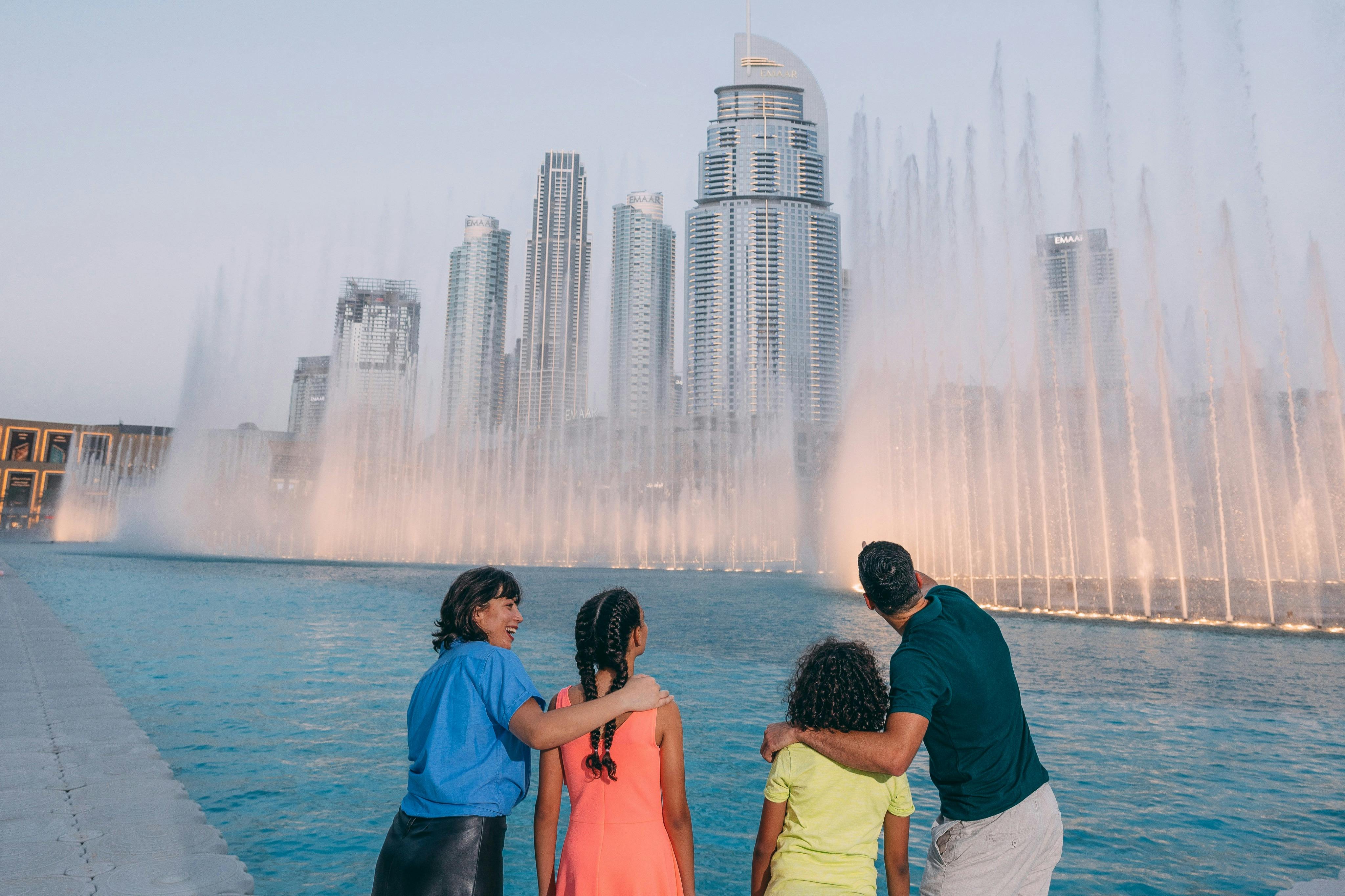 Čtyřčlenná rodina obdivuje fontánu u bazénu s vysokými městskými budovami v pozadí.