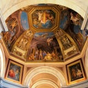 Un soffitto dettagliato e decorato con dipinti che raffigurano varie scene e figure mitologiche, incorniciato da un'architettura classica.