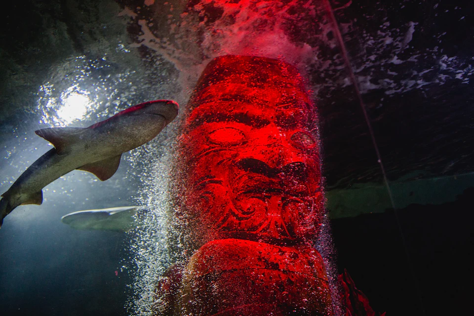 Large red statue head underwater with bubbles and a fish swimming nearby.