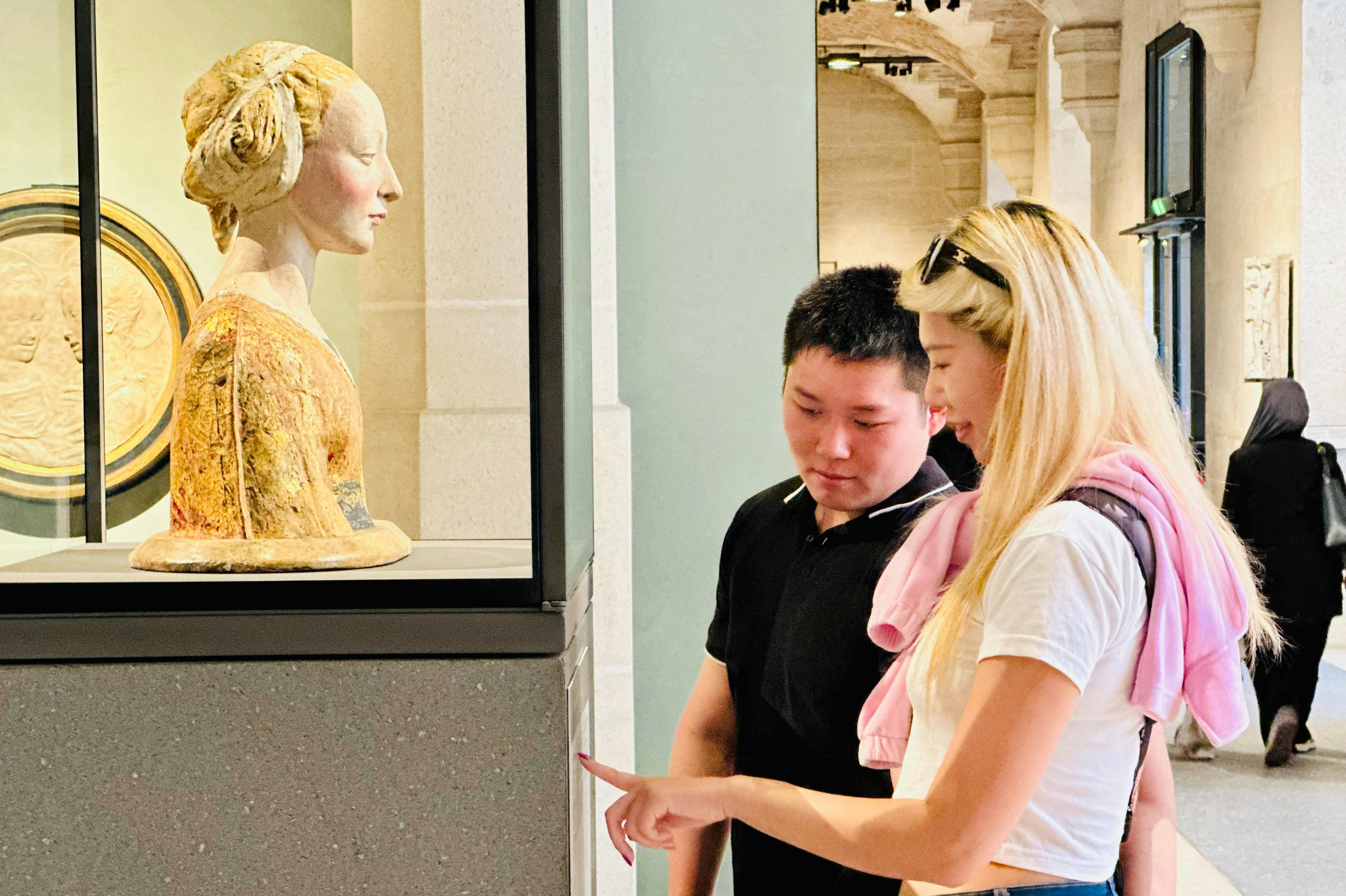 두 사람이 박물관에서 흉상을 살펴보고 있습니다. 유리로 둘러싸인 가슴은 여성의 프로필을 묘사합니다. 부부가 논의하거나 세부 사항을 지적합니다.