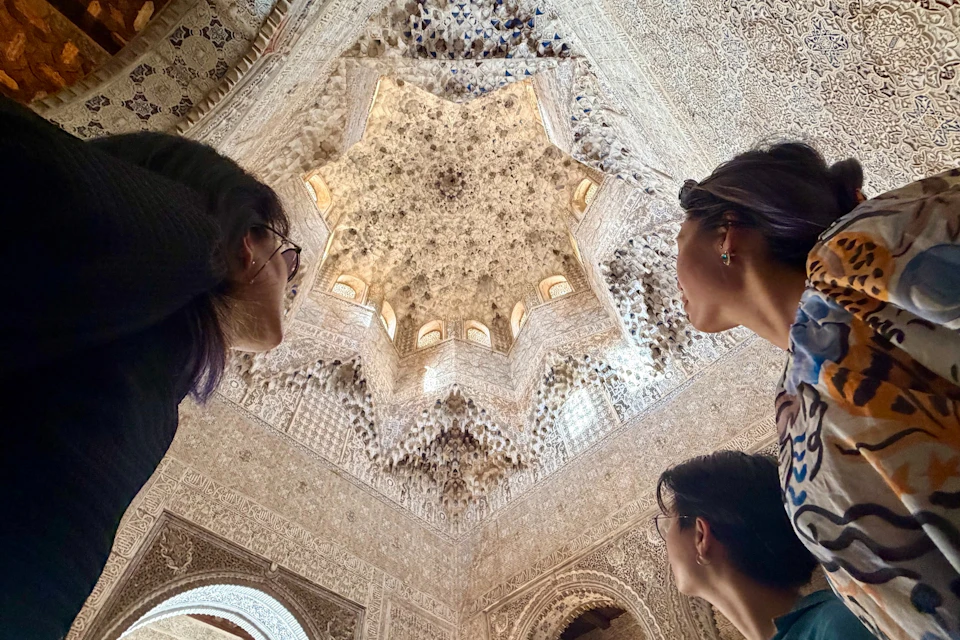 Three people look up at an ornate, intricately carved ceiling with a star-shaped central design and decorative details.