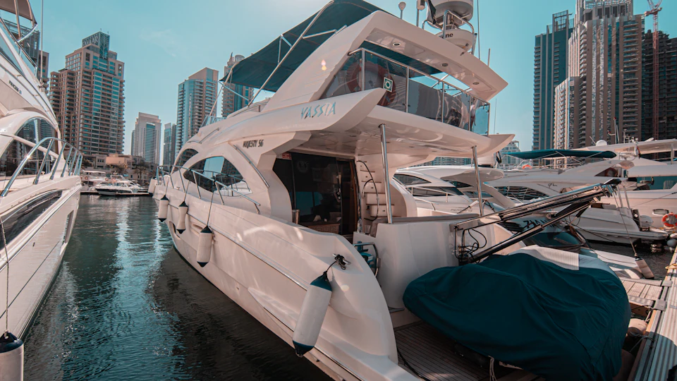 A white yacht named "Majesty 56" docked in a marina with modern buildings in the background.
