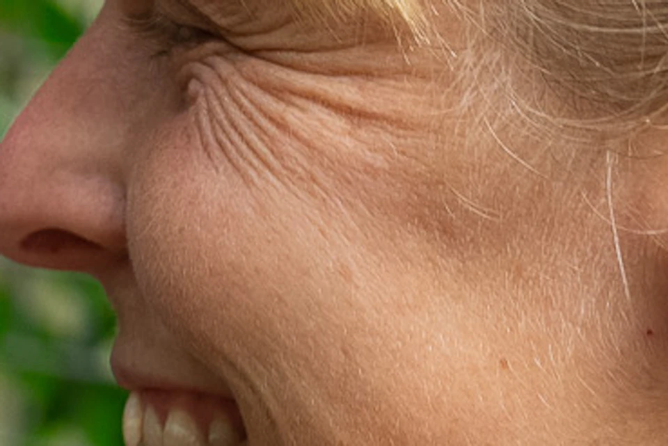 A woman and a sloth facing each other closely with a mesh fence and greenery in the background.