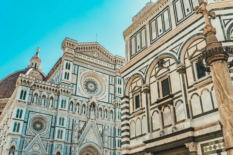 A view of Florence Cathedral's intricate facade and the adjacent Baptistery under a clear blue sky.