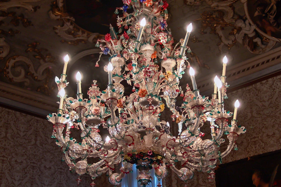 An ornate chandelier with intricate glass details and colorful decorations, lit candles in an elegant interior setting.