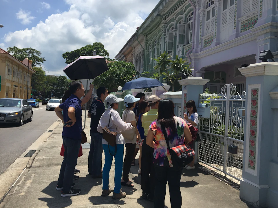 A group of people with umbrellas gather outside colorful row houses on a sunny day.